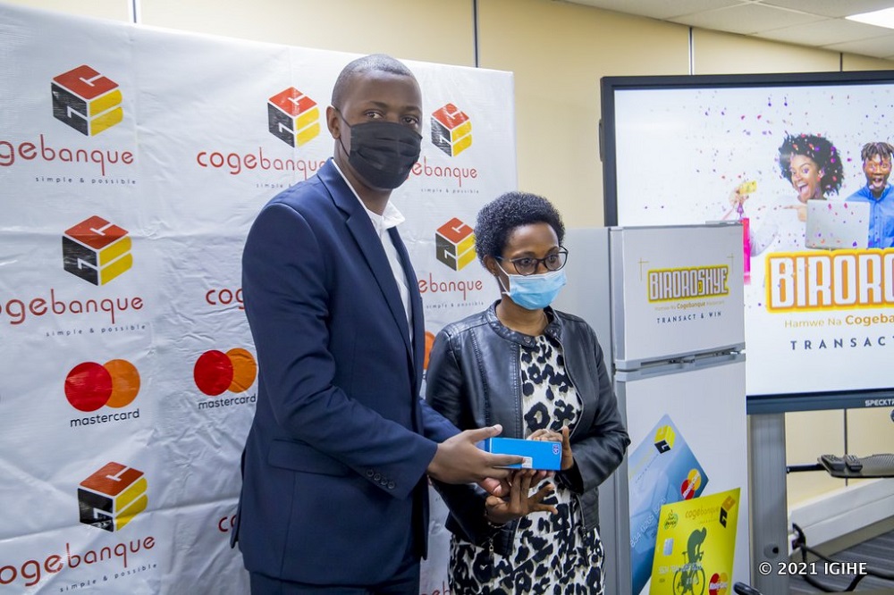 Umuyobozi ushinzwe Serivisi z'Ikoranabuhanga muri Cogebanque, Ndayambaje Raoul, ashyikiriza telefoni umwe mu bakiliya bakoresheje neza amakarita mu guhaha